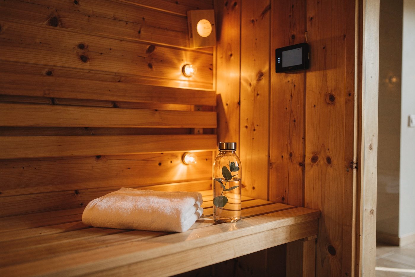 Cedar-paneled infrared sauna interior with warm amber bulbs, folded white towel and eucalyptus water bottle on the bench at Dr. Augello's Bethlehem PA practice.